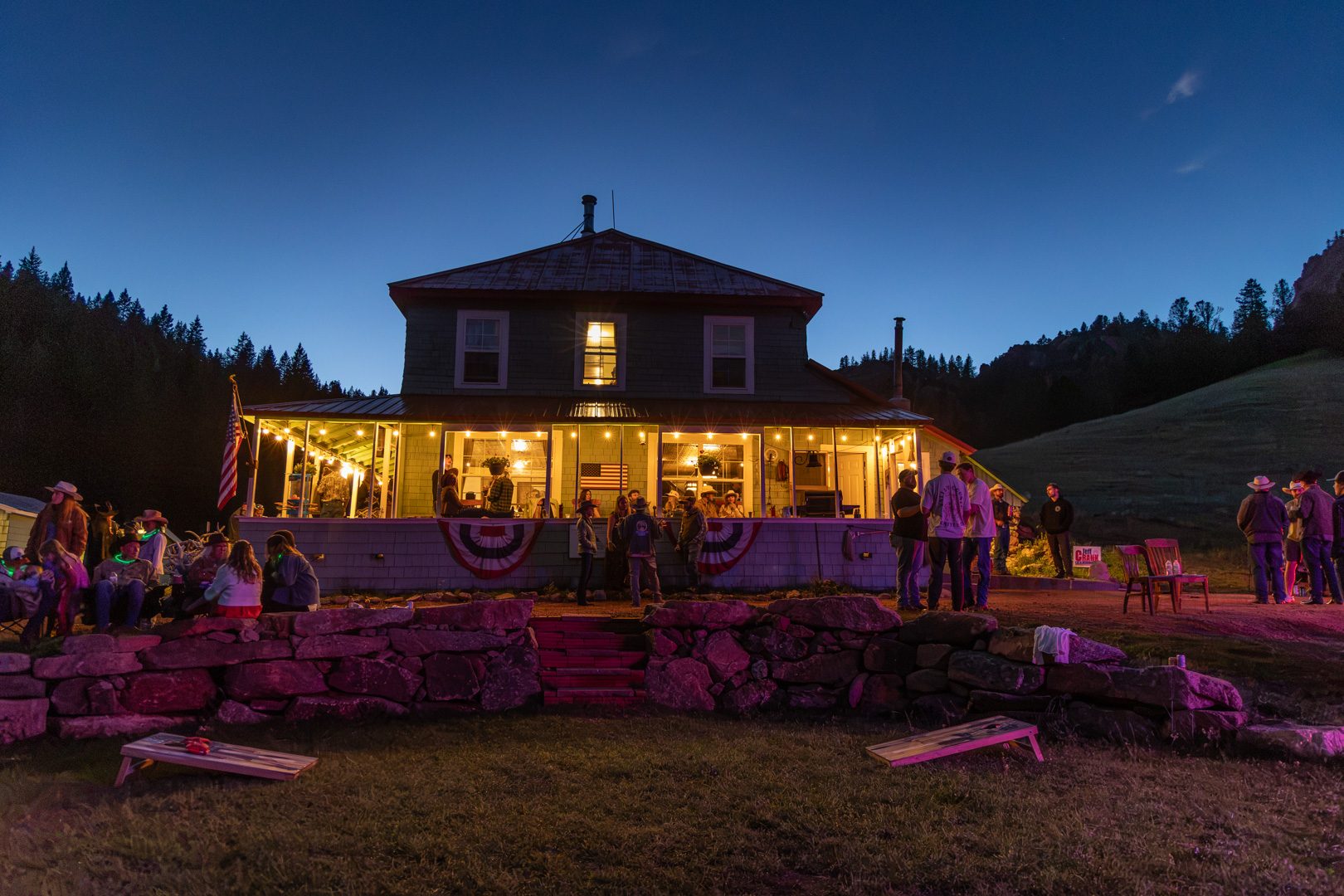 The Elk Glade lodge at dusk, porch lights on and guests on the lawn