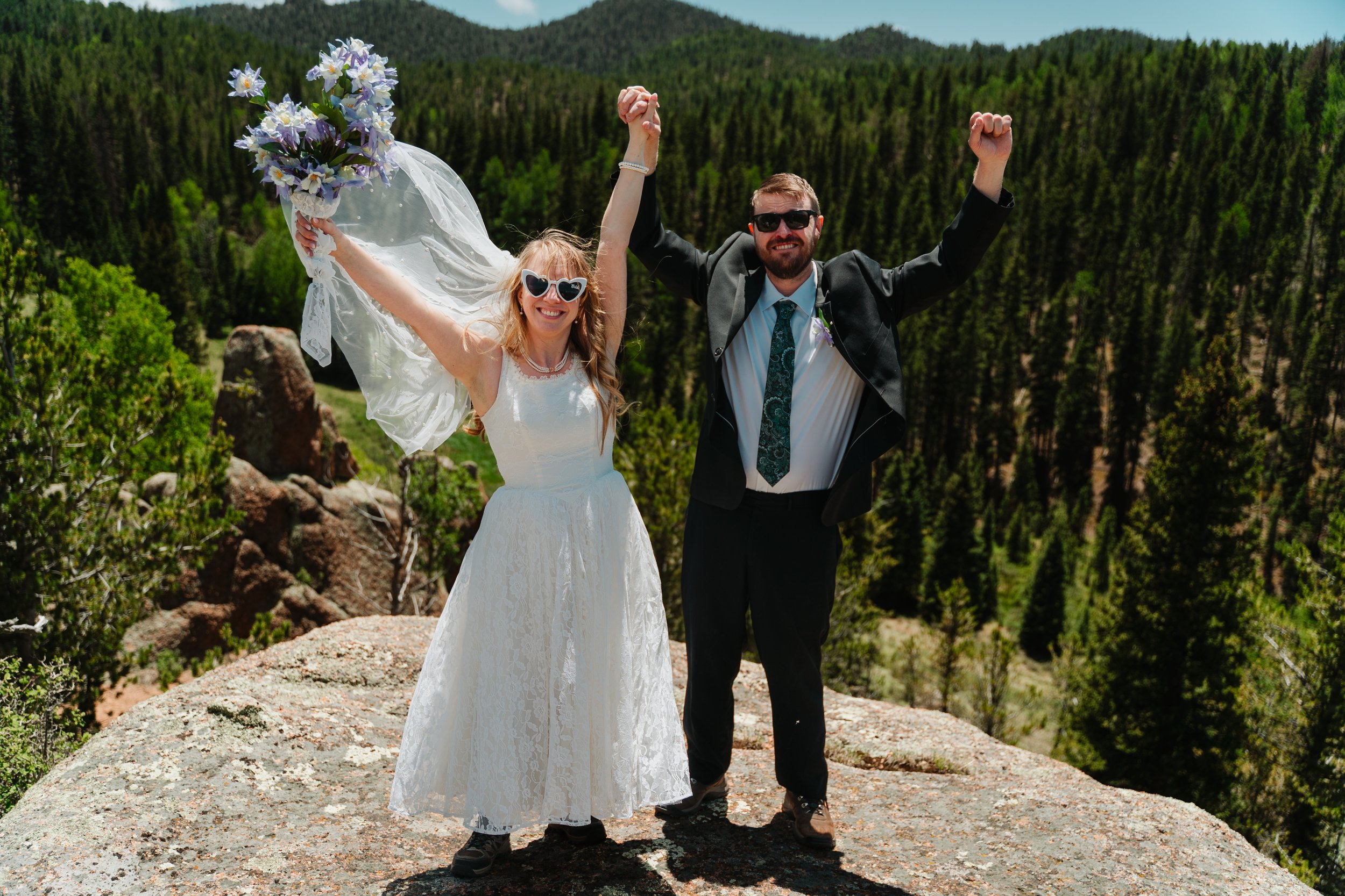 A bride and groom celebrating on a granite outcrop above the timber