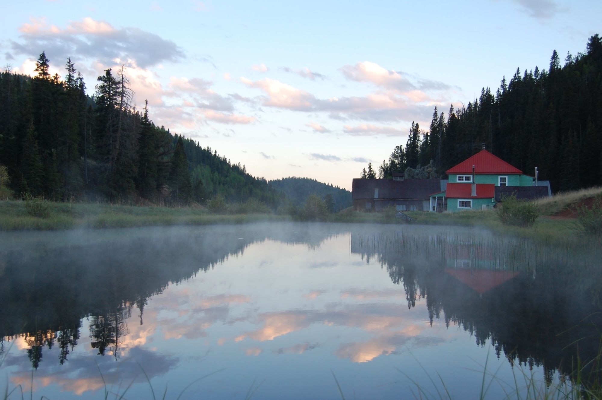 The red-roofed Elk Glade lodge beside a misty pond at dawn, pink clouds reflected in the water