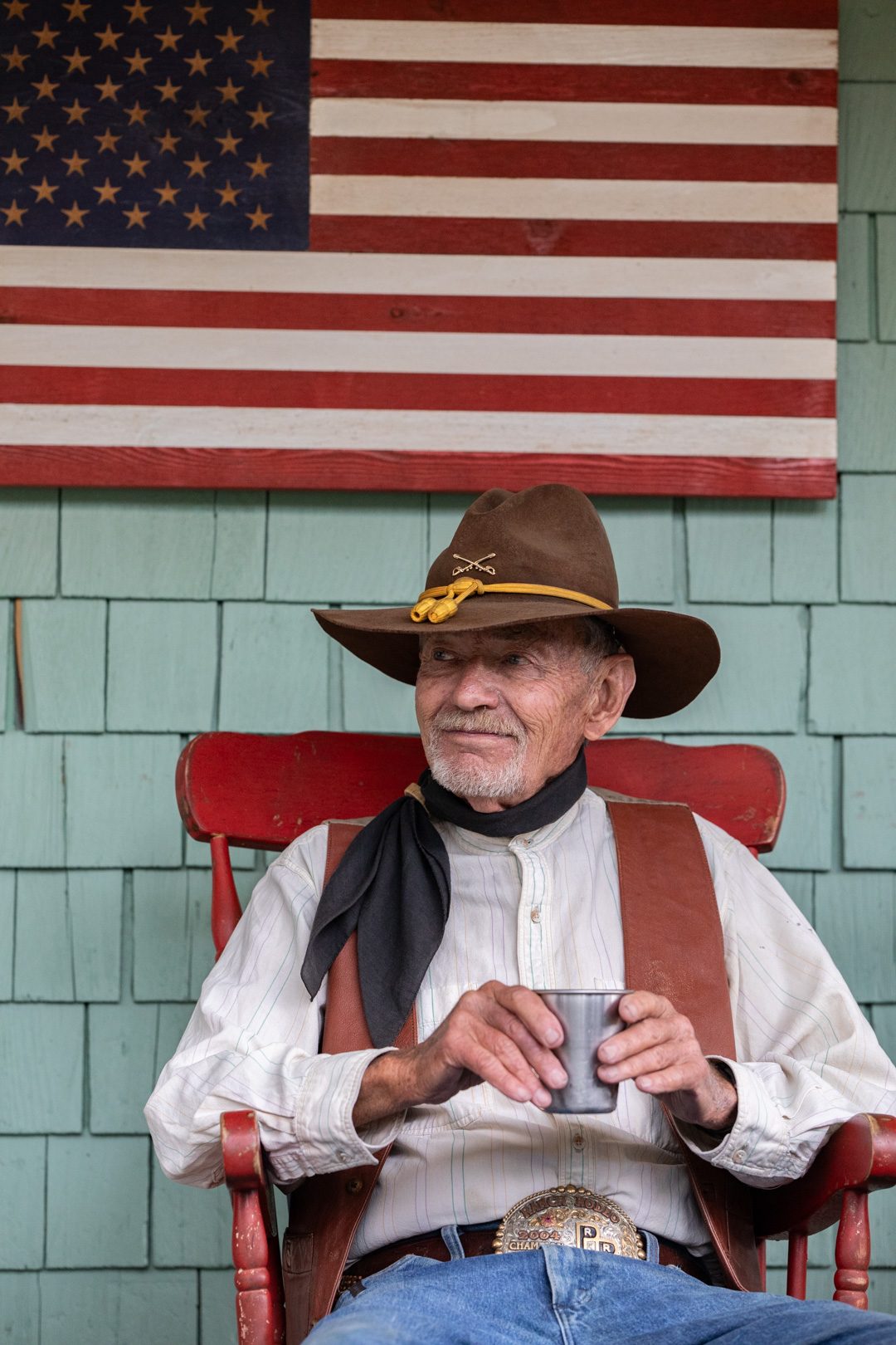 A cowboy in a red rocker under the flag on the lodge porch