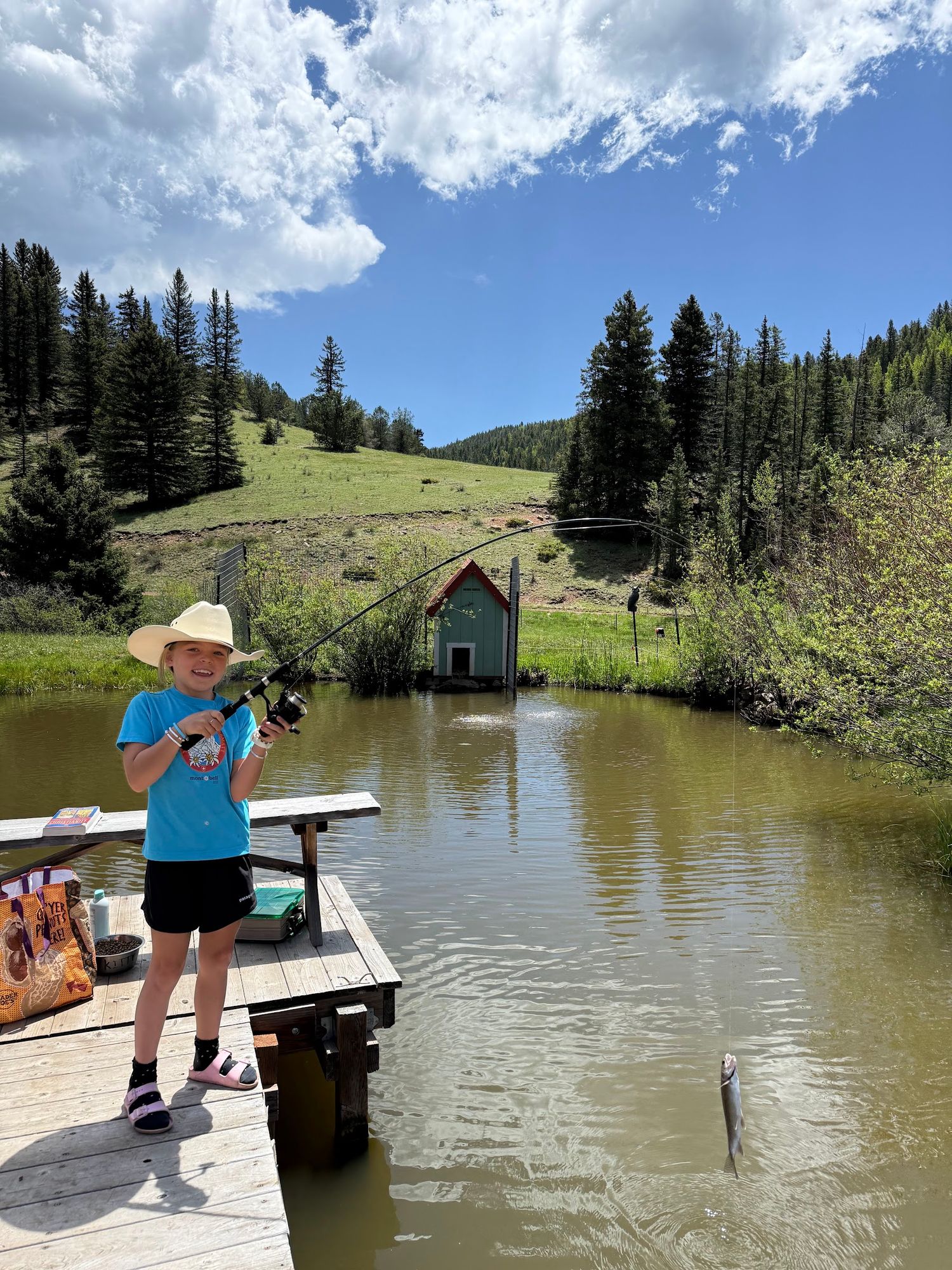 A young guest in a cowboy hat landing a trout off the dock on the ranch pond